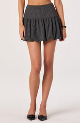 A woman is wearing a high-waisted, dark gray skirt with a subtle checkered pattern. The skirt features a gathered, bubble-style design with fabric that puffs out at the hem. She is also wearing black high-heeled shoes with a pointed toe and decorative buckle detail.